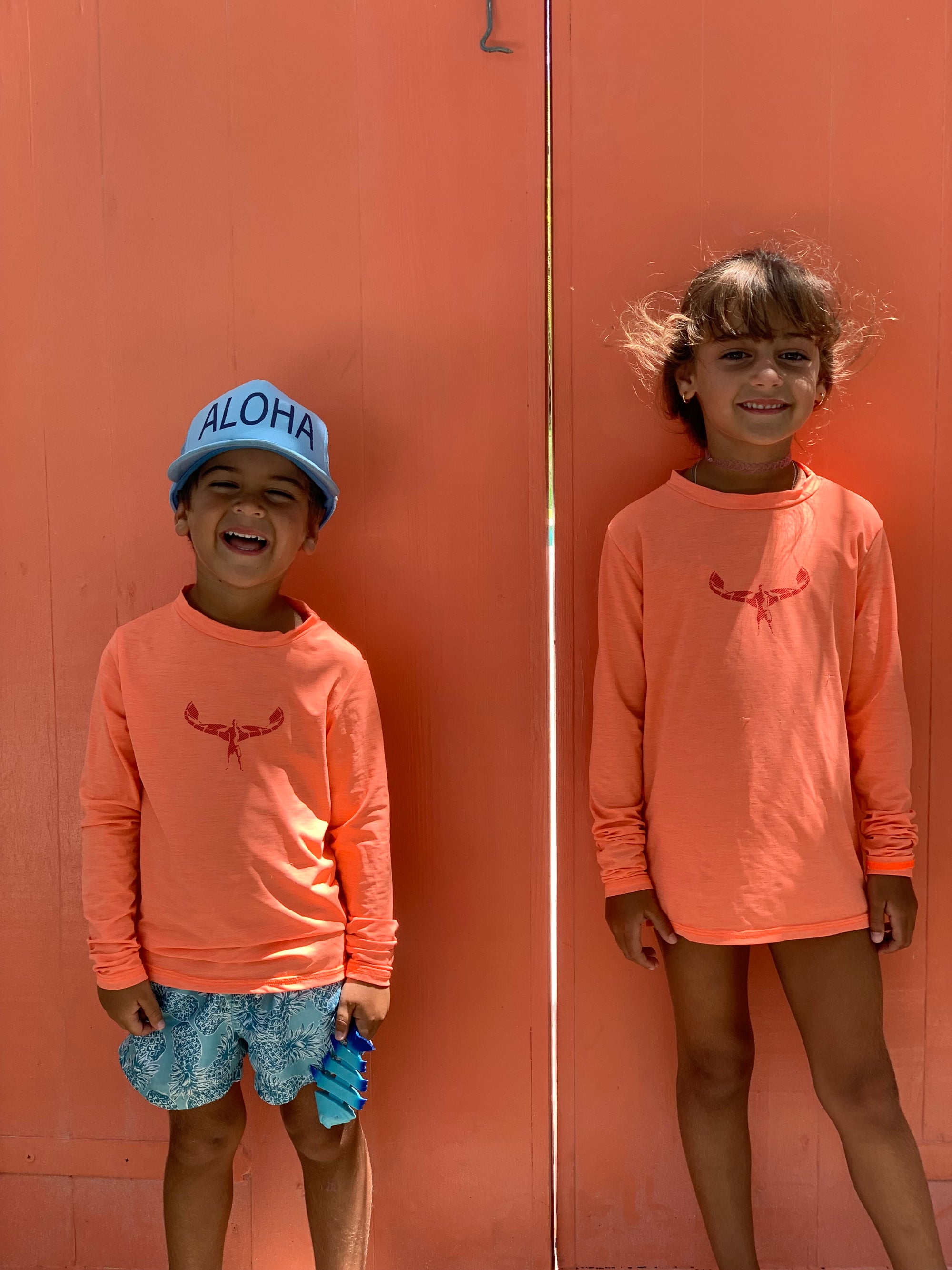 kids in front of an orange beach house door wearing TKSMIAMI rash guards and aloha hats